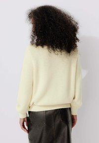 Pull tricoté jaune clair à coupe ample, épaules tombantes et poignets côtelés, associé à une jupe en cuir noir avec poches arrière.