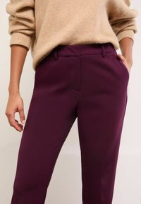 Pantaloni burgundy croiți, cu o textură netedă, având buzunare laterale și o croială slim; asortați cu un pulover din tricot bej.