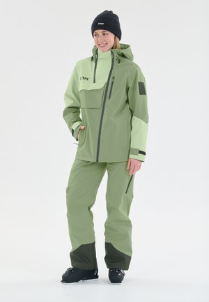 Groene en lichtgroene waterdichte jas met capuchon en zakken met rits, gecombineerd met bijpassende broek en zwarte laarzen. Voorzien van logo-accenten.