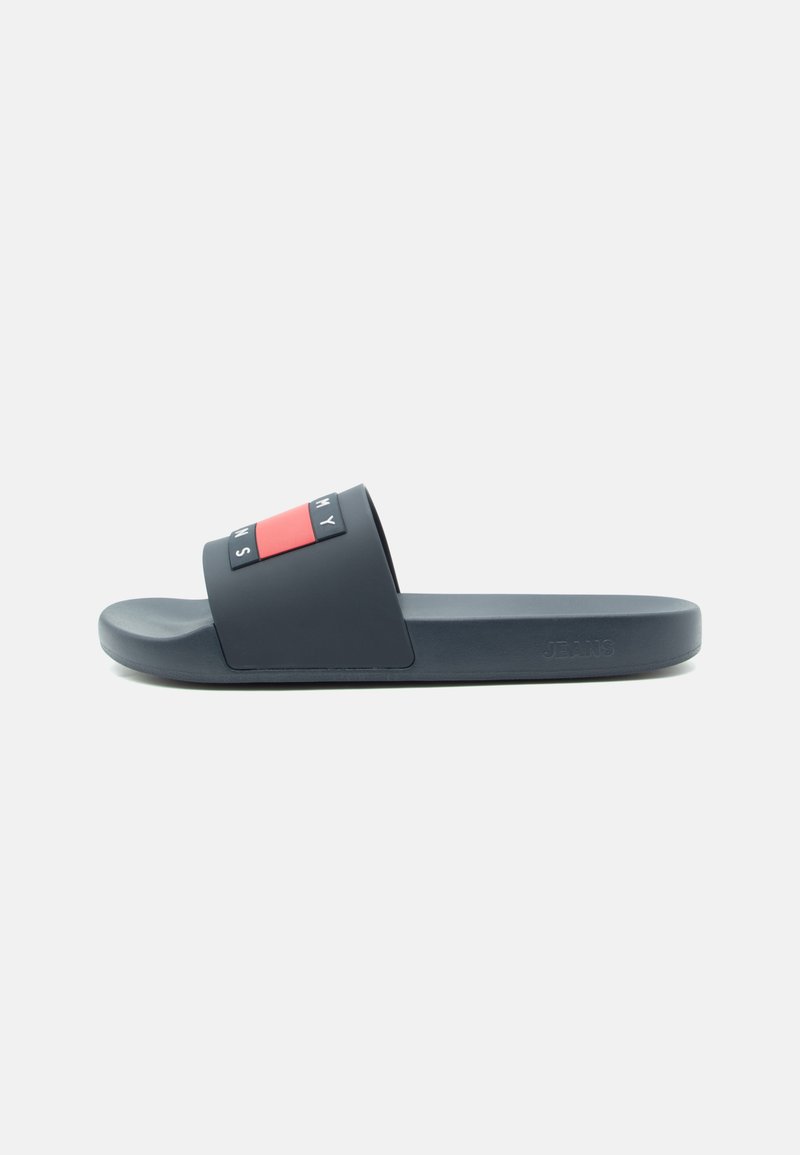 Sötétkék, slip-on szandál széles pánttal, piros és fekete téglalap alakú részletekkel, valamint a talpon lévő dombornyomott "JEANS" felirattal.