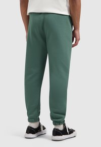 Groene joggers van een katoenmengsel met geribbelde boorden, een ontspannen pasvorm en een gladde textuur. Gecombineerd met zwarte sneakers en witte korte sokken.