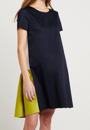 Kortærmet kjole med en marineblå overdel og en livlig grøn nederste panel med en glat tekstur og A-formet silhuet.