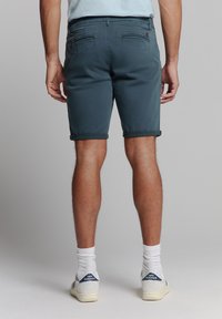 Heren teal shorts van een katoenmix, met een opgerolde zoom, achterzakken en gecombineerd met witte sokken en sneakers.