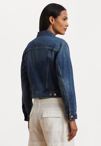 Τζάκετ τζιν σε σκούρο μπλε χρώμα με στενή γραμμή, μυτερό γιακά και κλείσιμο με κουμπιά. Διαθέτει διακριτική επένδυση και μακριά μανίκια.