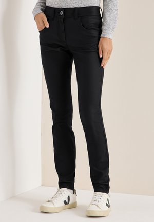 Černé slim-fit kalhoty vyrobené z hladkého materiálu, se předními kapsami, zapínáním na knoflík a čistou siluetou, doplněné bílými teniskami.