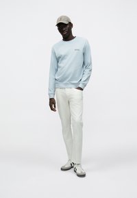 Ανοιχτό μπλε φούτερ με στρογγυλή λαιμόκοψη, λευκό παντελόνι και γκρι αθλητικά παπούτσια. Το καπέλο είναι μπεζ με κεντημένο λογότυπο. Λείο ύφασμα, άνετη εφαρμογή.