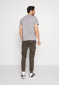 Grijze T-shirt met korte mouwen gecombineerd met olijfgroene cargobroek met zakken en een rood logo-tag. Zwart-witte sneakers maken de look compleet.