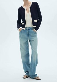 Cardigan bleu marine avec accents crème, boutons dorés, assorti à un jean large bleu clair et des sandales noires. Design simple et coupe décontractée.