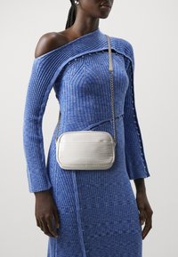 Modrá žebrovaná šaty s designem bez ramínek a detaily s knoflíky; v kombinaci s bílou kabelkou ve stylu faux-krokodýl na řetízkové šle.