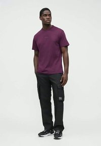 Bordó bavlněné tričko s kulatým výstřihem, v kombinaci s černými nákladními kalhotami s kapsami a černými teniskami s bílými detaily.