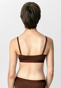 Braune gerippte Bralette mit verstellbaren Trägern und einem breiten Bund. Glatte Textur und einfaches Design, von hinten betrachtet.
