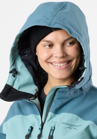 Light blue and dark teal waterproof jacket with a hood, featuring adjustable cords and a logo on the chest. Textured fabric with zippers.