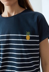 Marineblauw katoen t-shirt met witte horizontale strepen en een kleine gele geborduurde ananas op de borst, ronde halslijn en korte mouwen.