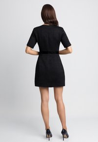 Czarna sukienka o teksturowanym wykończeniu, z krótkimi rękawami, dopasowana w talii, z aksamitnym akcentem na plecach. W zestawie z czarnymi, wysokimi szpilkami.