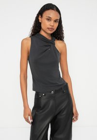 Mouwloze, donkergrijze top met gedraaide knoopdetail bij de halslijn en een gladde textuur, gecombineerd met zwarte, losse leren broek.