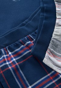 Gros plan de trois tissus pliés avec des ceintures élastiques : bleu marine uni, bleu marine à carreaux rouges et blancs, et gris clair à fines rayures rouges et noires.