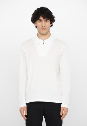 Langærmet hvid polo skjorte med lynlås krave, der har et struktureret stof og et klart V-formet design på brystet.