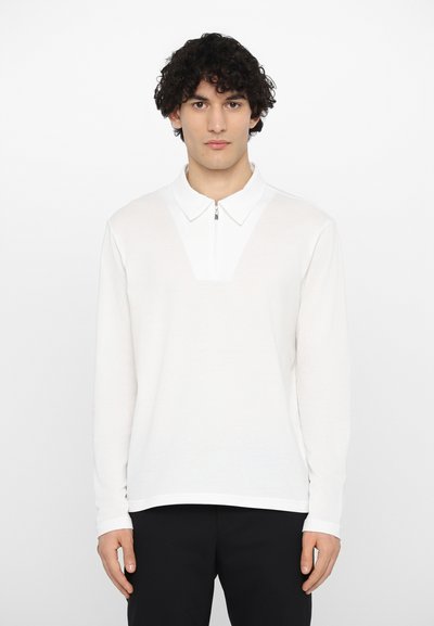 Langermet hvit polo med glidelås på kragen, med teksturert stoff og et distinkt V-formet design på brystet.