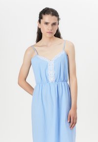 Light blue sleeveless dress with a V-neck, featuring white lace trim down the front and an elastic waist for fit. Smooth fabric texture.