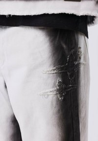 Jeans de mezclilla desgastados en un degradado de blanco a negro, con bordes deshilachados y dos patrones de cruces bordados en el muslo.