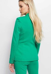 Groene blazer met een getailleerde fit, schoudernaden en drie knoopaccenten op de manchetten, gecombineerd met bijpassende broeken. Gladde textuur.