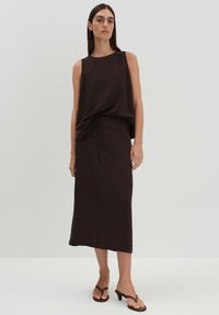 Haut sans manches brun assorti à une longue jupe brune, avec une texture lisse et un design simple. Le mannequin porte des tongs noires.