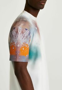 Tričco s krátkým rukávem s gradientním designem zahrnujícím oranžové, fialové a modré skvrny na bílém podkladu. Hladká textura, moderní střih.