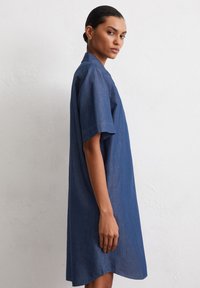 Denim jurk met korte mouwen, kraaghalslijn en een losse pasvorm. Donkerblauwe kleur en subtiele textuur. Zoom eindigt boven de knie.