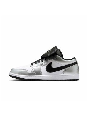 Sneaker basse avec panneaux blancs et argentés, logo Swoosh noir, lacets noirs et languette noire relevée sur fond blanc.