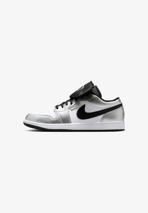 Sneaker basse avec panneaux blancs et argentés, logo Swoosh noir, lacets noirs et languette noire relevée sur fond blanc.