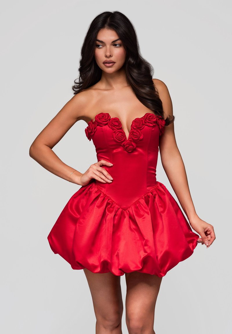 Röd satin klänning med en djup V-ringning prydd med ros-applikationer, en figurnära bodice och en voluminös, rynkad kjol nedanför.