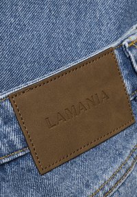 Pruun nahast silt, millel on reljeefselt peal "LAMANIA", on sinise teksariide peale õmmeldud kollase õmblusega.