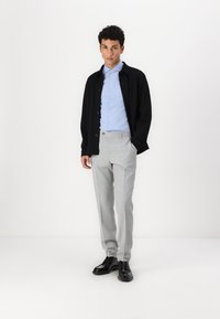 Veste noire à boutons, chemise bleu clair, pantalon à carreaux gris, et chaussures noires. Le tissu semble lisse ; design ajusté avec une silhouette moderne.