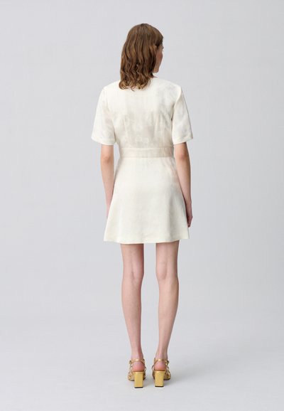 Robe blanche à manches courtes avec une taille cintrée et une jupe évasée, présentant un motif floral subtil. Assortie à des sandales à talons blocs jaunes.