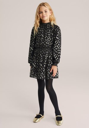 Fekete ruha begyűrt nyakkivágással és hosszú ujjakkal, ezüst leopárdmintával. A szoknya réteges fodrokkal díszített. Fekete harisnyával és aranycipővel párosítva.