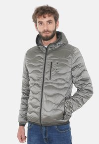 Giacca imbottita grigia con cappuccio, trama a onde, chiusura con zip e tasca sul petto. Stile casual, adatta per uso all'aperto.