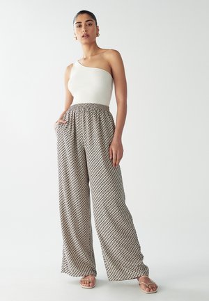 Asymmetrical cream ribbed top paired with wide-leg patterned pants in beige and black, featuring an elastic waistband and side pockets.