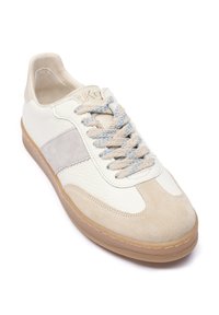 Bela in bež superga z zgornjim delom iz teksturirane usnjene in semiš usnja, okrogla sprednja stran in svetlo modri čevlji. Gumijast podplat z rjavim poudarkom.