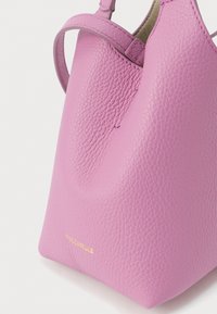 Μικρή ροζ τσάντα χειρός από δερματίνη με υφή, με καμπυλωτές λαβές στην κορυφή και χρυσή ανάγλυφη ονομασία της μάρκας «Coccinelle» στο κάτω δεξί μέρος.