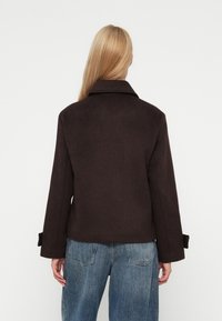 Chaqueta de mezcla de lana marrón oscuro con cuello con solapa, mangas amplias y puños ajustables, combinada con jeans de talle alto azul claro.