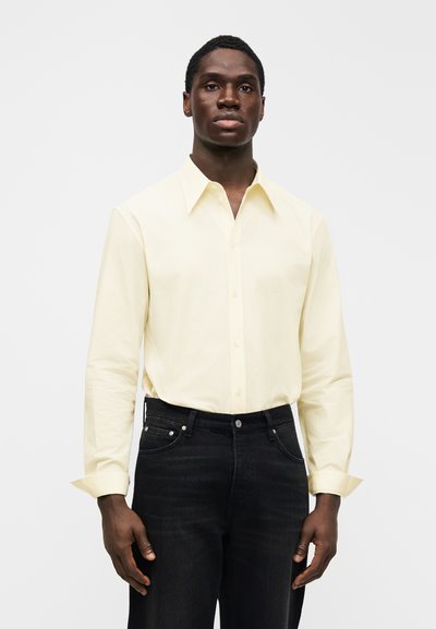 Jasnożółta koszula na guziki z kołnierzem typu spread i długimi rękawami, w zestawie z czarnymi jeansami o klasycznym kroju z pięcioma kieszeniami.