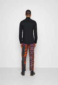 Camicia nera a maniche lunghe abbinata a pantaloni dai motivi astratti colorati in arancione, viola e grigio. Scarpe nere completano il look.