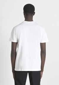 Camiseta blanca de algodón con mangas cortas, cuello redondo y corte recto. La vista trasera muestra costuras mínimas y sin gráficos o logotipos visibles.