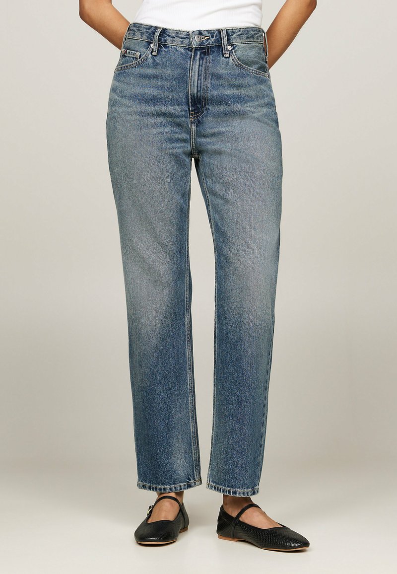 Kõrge vöökohaga sinised denim teksad sirge lõikega, klassikalise viie taskuga disain ning kerge tuhmumine. Kombineeritud mustade lamedate kingadega.