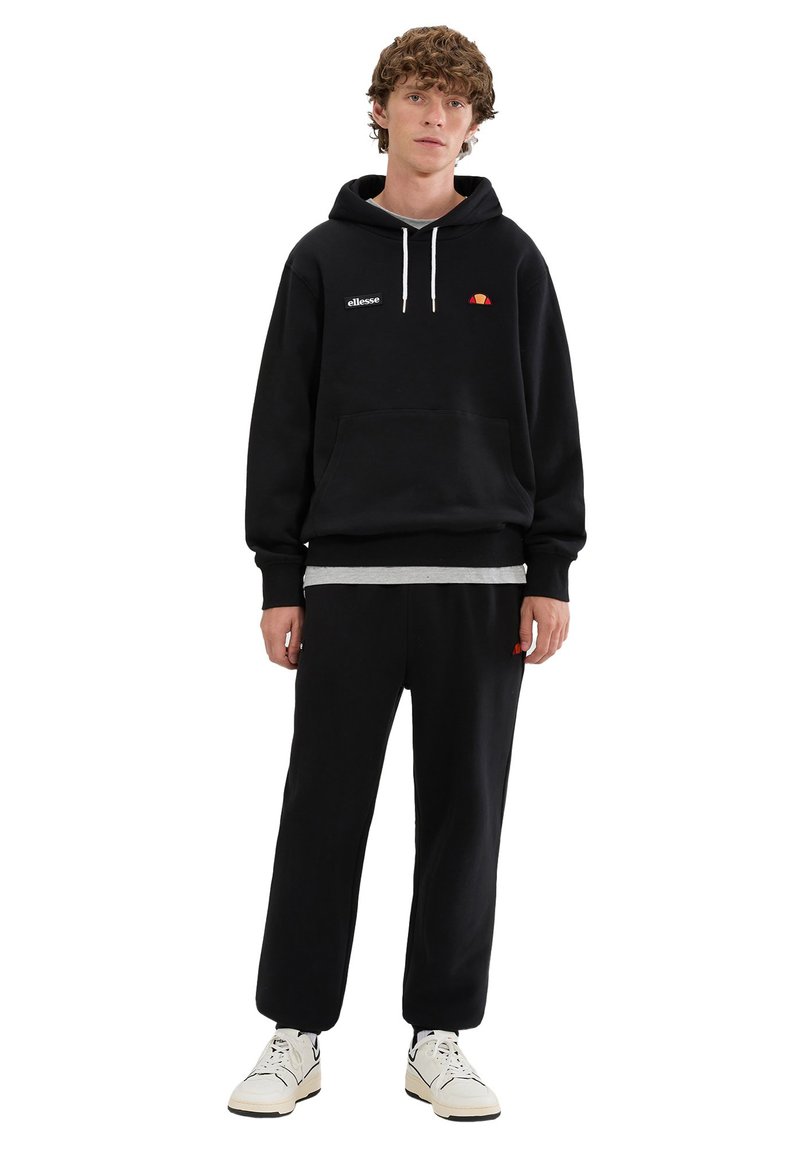 Sudadera con capucha negra hecha de mezcla de algodón, con bolsillo tipo canguro y logo bordado. Combinada con pantalones jogger negros a juego y zapatillas.