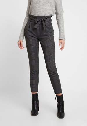 Woman wearing high-waist grey plaid pants with a tied fabric belt, grey sweater, and black heeled ankle boots, standing against a white background.