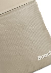 Light beige backpack with hexagonal texture, featuring a top zipper and a white logo. Material appears durable and waterproof.