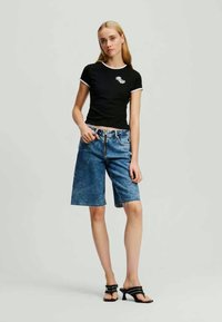 Melna pieguļošā T-kreklus ar baltu apdari, apvienots ar ziliem džinsu Bermudu šortiem. Regulējama jostasvieta, teksturēta auduma, un minimālisma dizains.