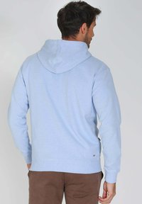 Sweatshirt à capuche bleu clair avec des manches longues, des poignets et un ourlet côtelés, et un petit logo près de la couture, fabriqué en tissu doux.
