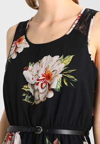 Schwarzes Blumenkleid mit großen weißen und roten Blumen, Spitzen-Schulterdetails und einer taillierten Taille mit einem schwarzen Gürtel. Glatte Stofftextur.
